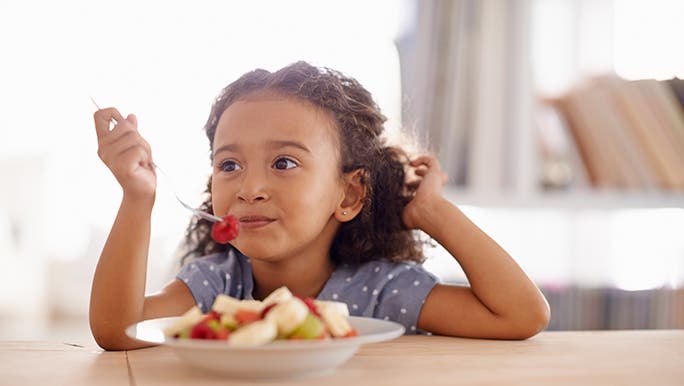 A kid eats a bowl of fruit salad for breakfast, she looks happy. 