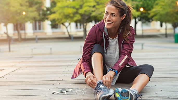 Woman sitting down and adjusting her shoes before going for a run