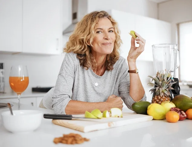 Woman in her kitchen leaning on the bench snacking on fruits and nuts