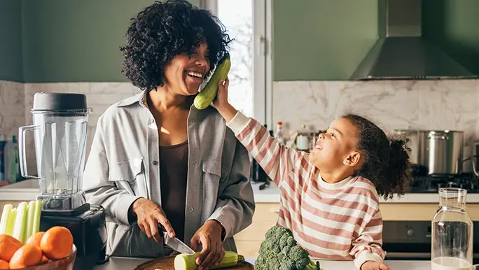 Mother and daughter are in the kitchen shopping up fresh vegetables, which are full of goodness to help support your gut health.