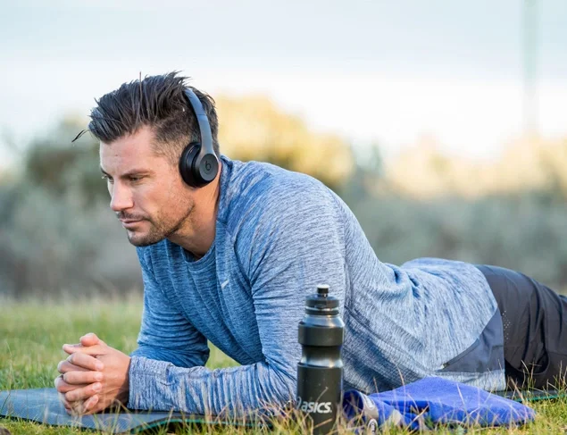Sam Wood relaxing and listening to music on a yoga mat outside on the grass