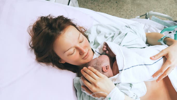 A mother holds her newborn in a hospital bed. It’s natural for births to not go to plan but they look happy. 