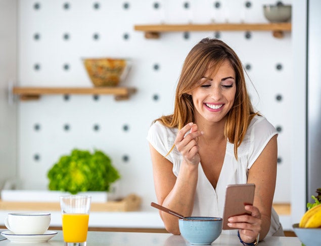 Woman snacking in her kitchen and looking at her smartphone