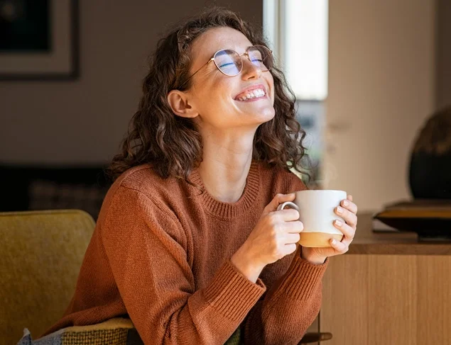 Smiling pretty girl drinking hot tea in front of the window in winter.