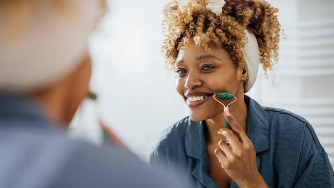 A woman is smiling as she uses a jade roller on her face