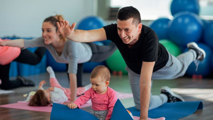 A man is doing stretches on a yoga mat as part of a group exercise class with his baby and he hopes to do some lower back stretches.