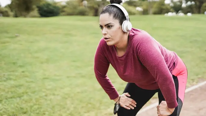 Woman taking a rest while out running, listening to music through headphones
