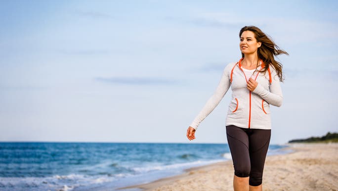 Woman with long brown hair walking along the beach in active wear