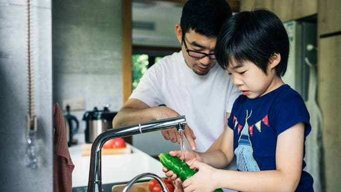 A father is teaching his son how to wash vegetables.