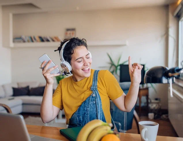 Relaxed young woman singing along to music she is listening too through headphones while working from home