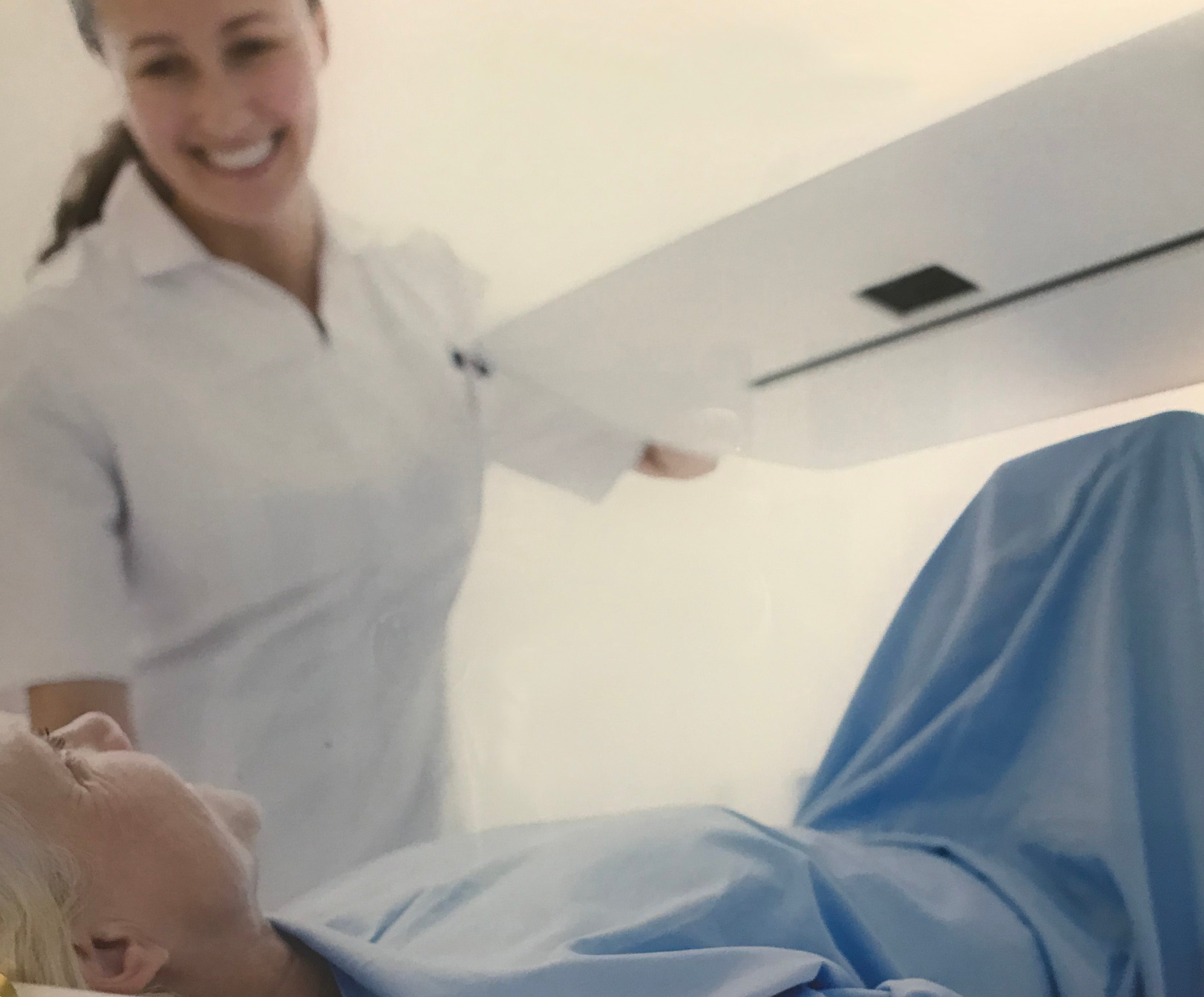 A smiling R.T. in white scrubs comforts a patient in a Bone Densitometry scanner