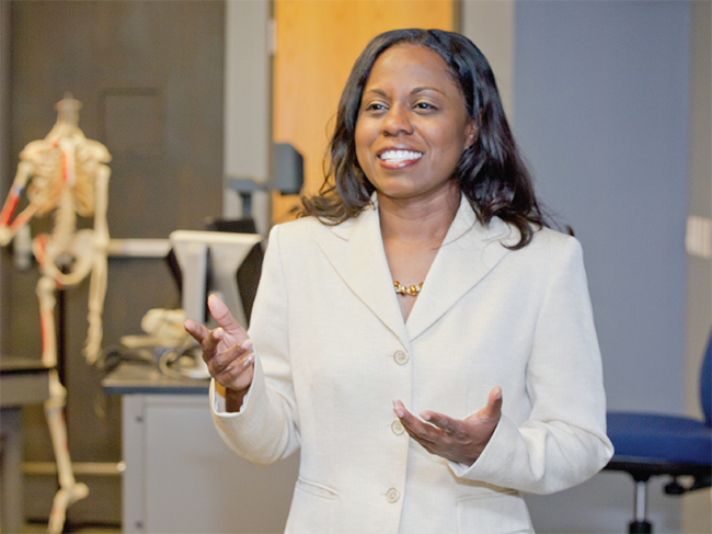 In the foreground; a smiling female educator in a white suit jacket; in the background, a skeleton