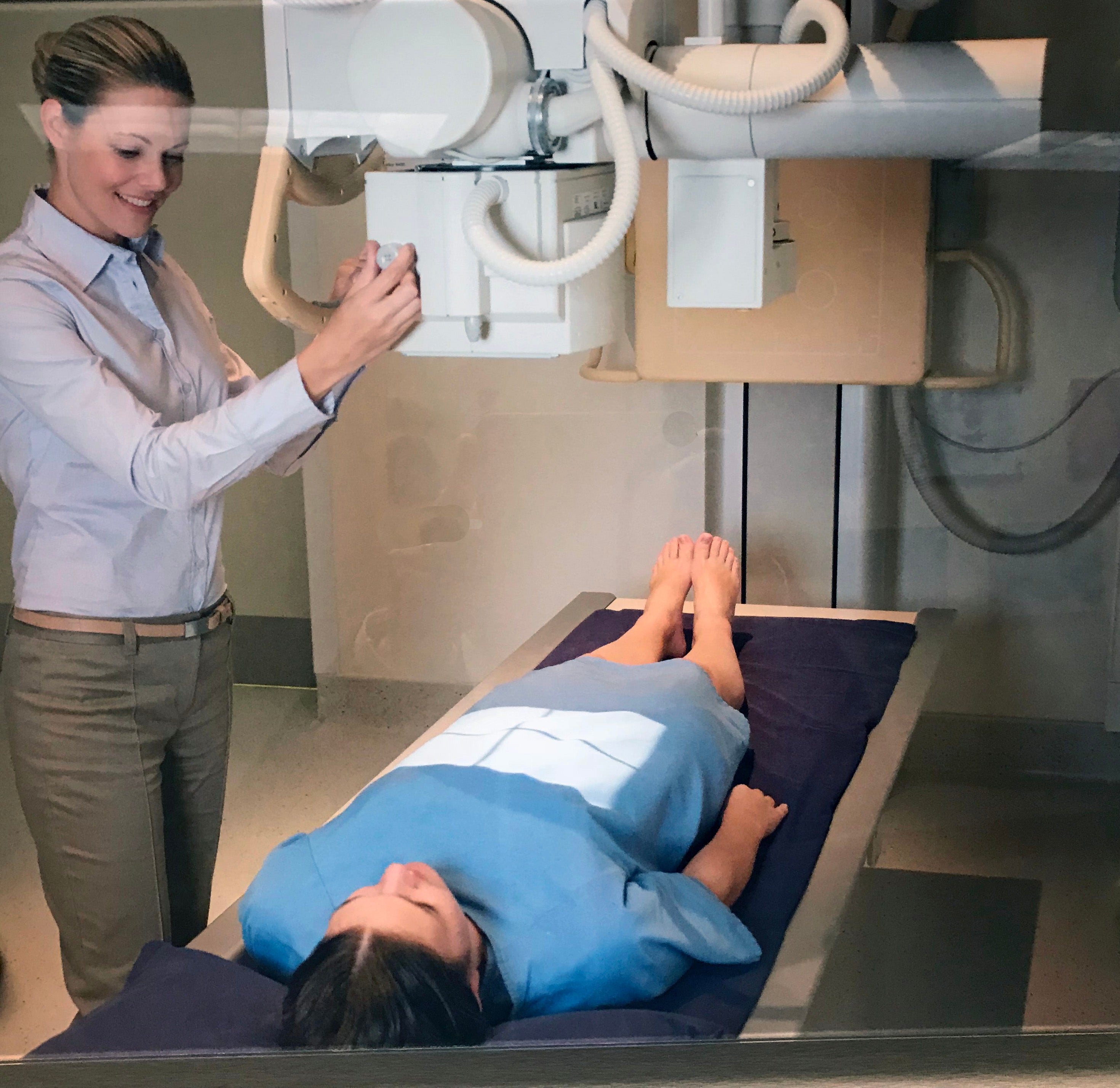 A female patient is laying on an X-ray table, prepping for an abdominal X-ray.