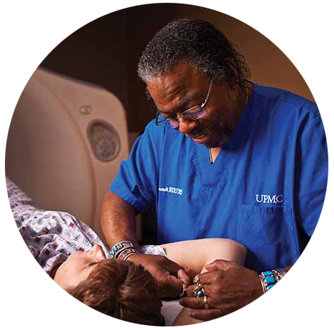 Round photo of a male R.T. in blue scrubs comforting a patient on a scanner bed