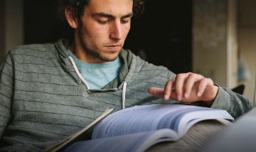 A student wearing a gray-striped sweatshirt studying with a textbook.