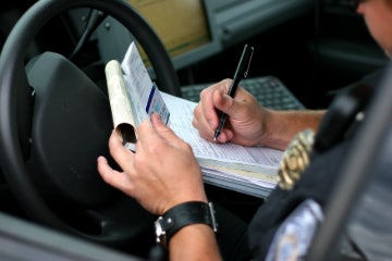 A police officer sitting in a car, writing a ticket.