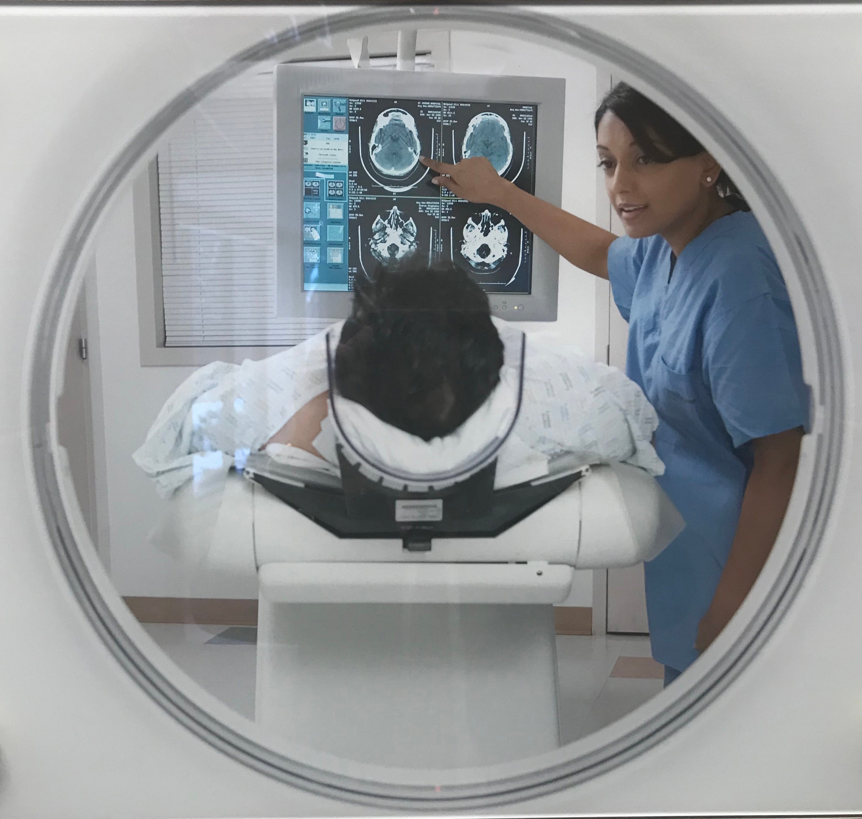 A patient laying on a CT scanner bed while an R.T. points at images on a monitor.