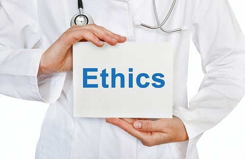 A medical professional wearing a white lab coat and a stethoscope holding a white placard that says "Ethics" in blue type