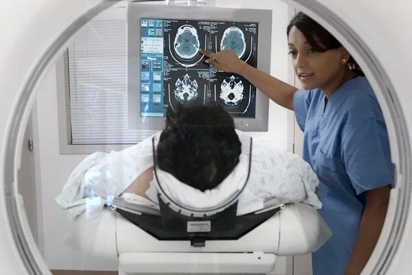 A patient laying on a CT scanner bed while an R.T. points at images on a monitor.