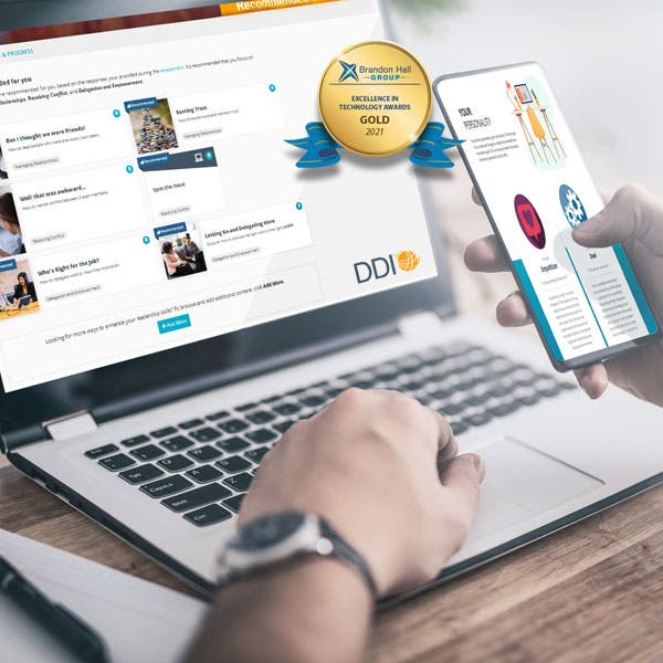 Person typing on laptop and scrolling through an app on their phone, both devices running DDI's Leadership Development Foundation Subscription. ?auto=format&q=75
