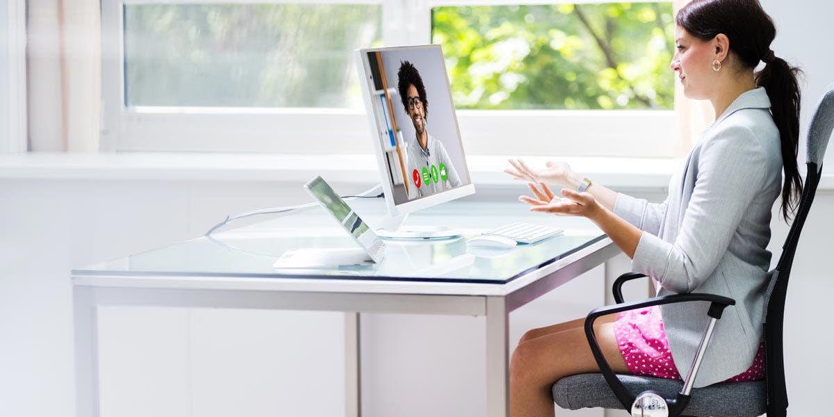 Woman demonstrating virtual leadership skills as she participates in a virtual conference call while wearing a professional suit jacket on top and pink boxer shorts on bottom