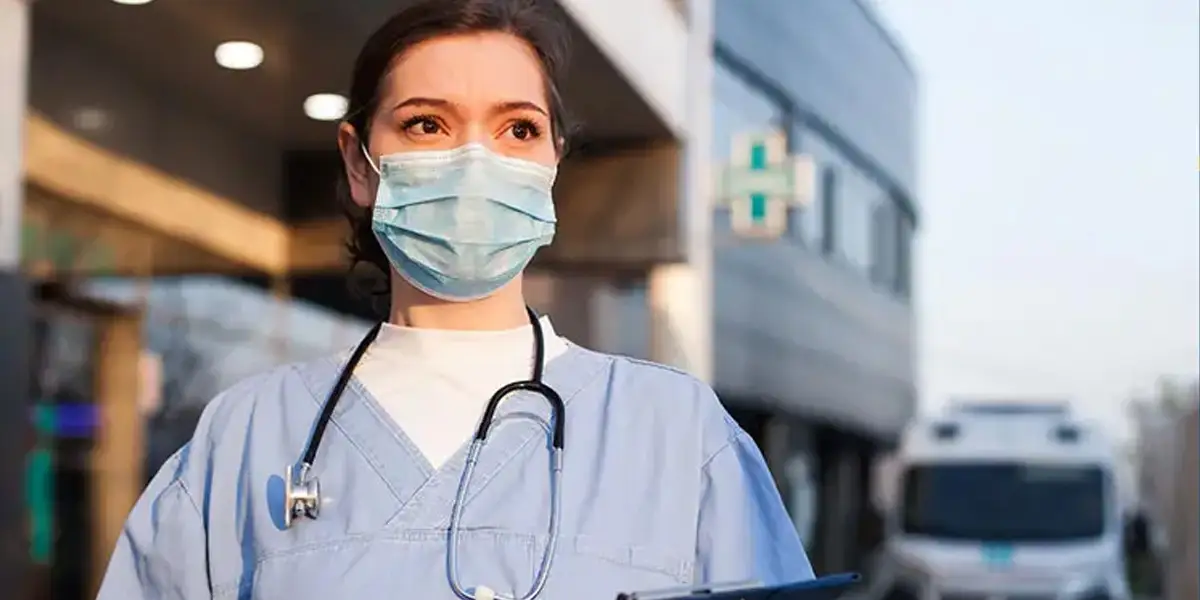 nurse with a mask on standing in front of the hospital she works at