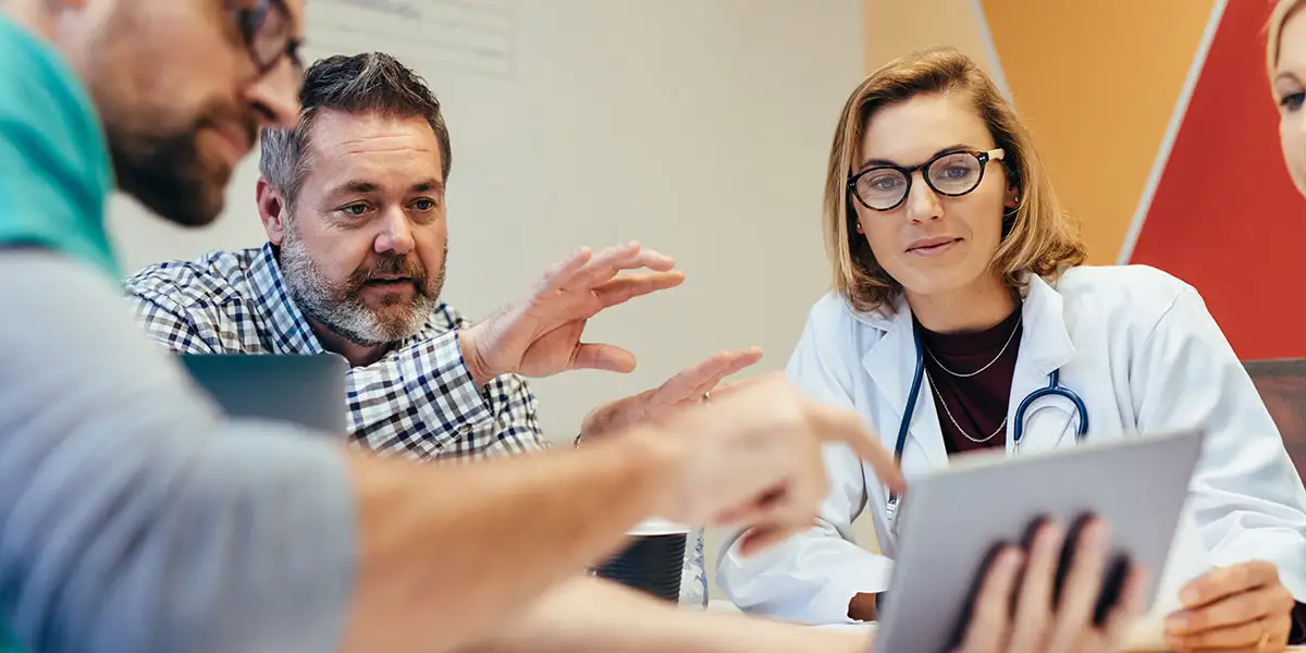 A female medical professional sitting with 2 males looking at a table to represent interviewing in a virtual setting