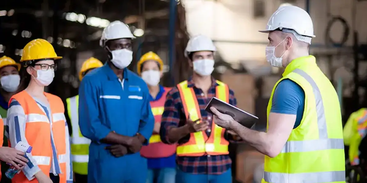 a group of manufacturing workers listening to their manufacturing leader talk to them on the manufacturing floor