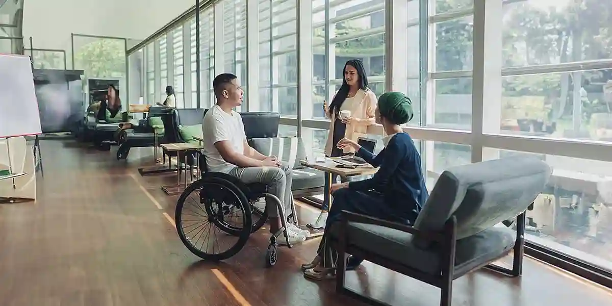 man in a wheelchair talking to two other colleagues in the office about diversity, equity, and inclusion