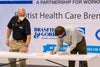 Man bent over signing a paper with another man onlooking