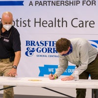 Man bent over signing a paper with another man onlooking