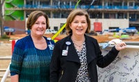 Cyd Cadena Senior VP and Julie Cardwell Senior VP take photo in front of topping off construction beam.
