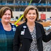 Cyd Cadena Senior VP and Julie Cardwell Senior VP take photo in front of topping off construction beam.