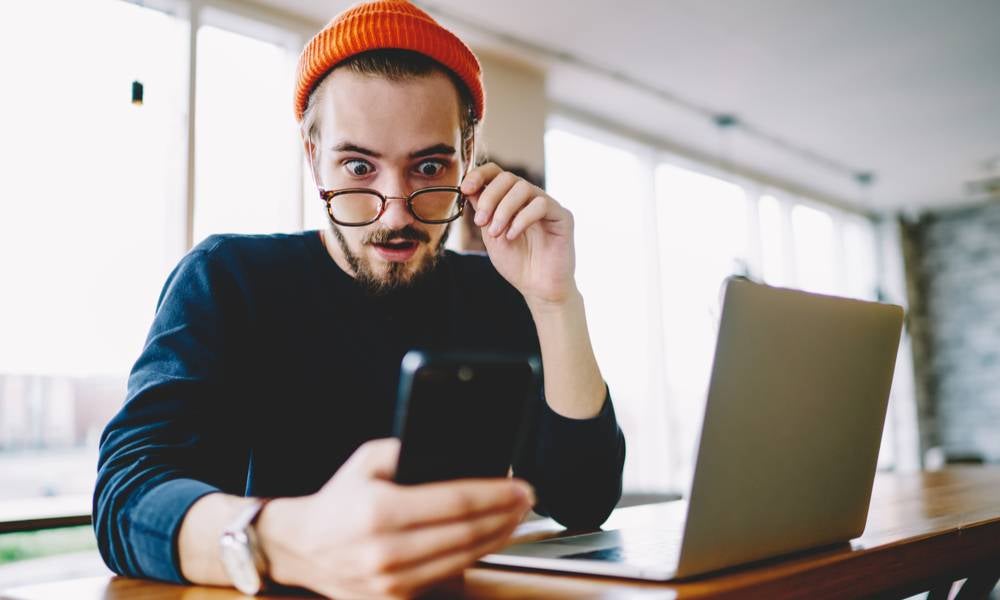 Man reading news on his phone looks shocked and suprised.jpeg