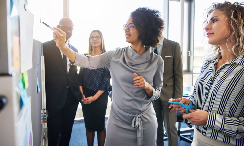 Diverse group of focused businesspeople brainstorming together on a whiteboard during a strategy session in a bright modern office.jpeg