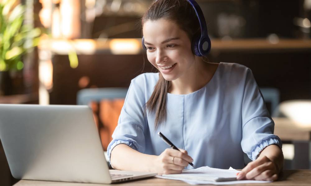 Smiling student wears wireless headphone study online with skype teacher, happy young woman learn language listen lecture watch webinar write notes look at laptop sit in cafe, distant education.jpg