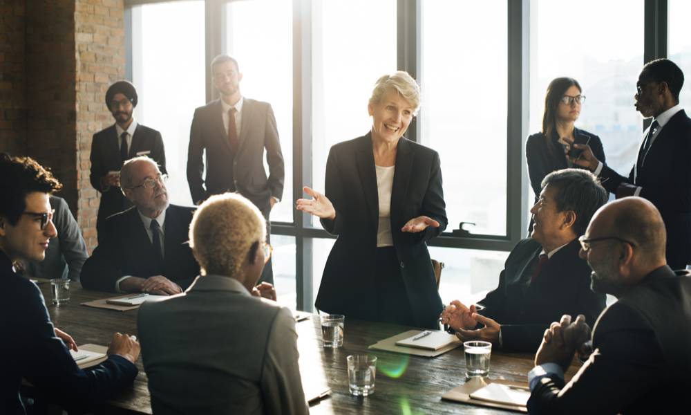 Woman speaks during a boardroom meeting to a crowd of mostly men.jpeg