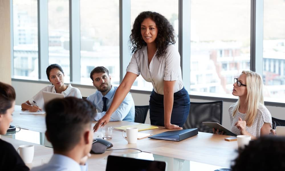 Business woman standing up talking in a meeting paradoxical leadership.jpeg