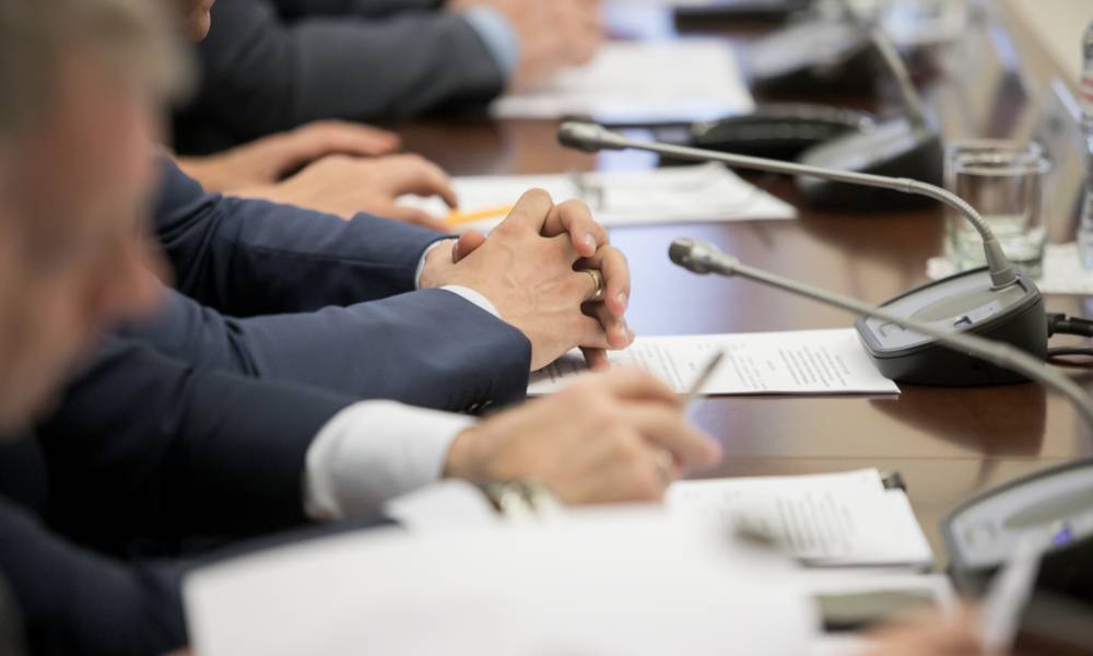 Politicians sitting by table with their hands over documents.jpg