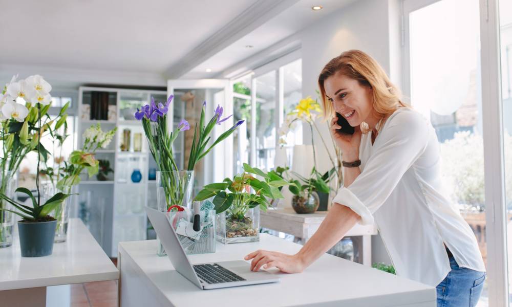 Female florist standing at her flower shop counter using mobile phone and laptop to take orders for her store (1).jpg