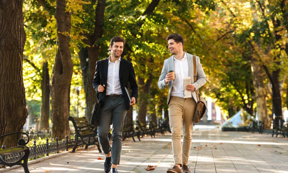 businessmen in suits walking outdoor through green park with takeaway coffee and laptop during sunny day.jpeg