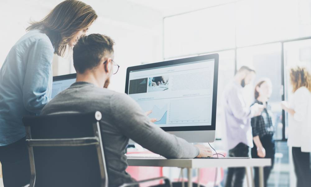 Manager shows coworker new ideas on a monitor with employees in the distance.jpg