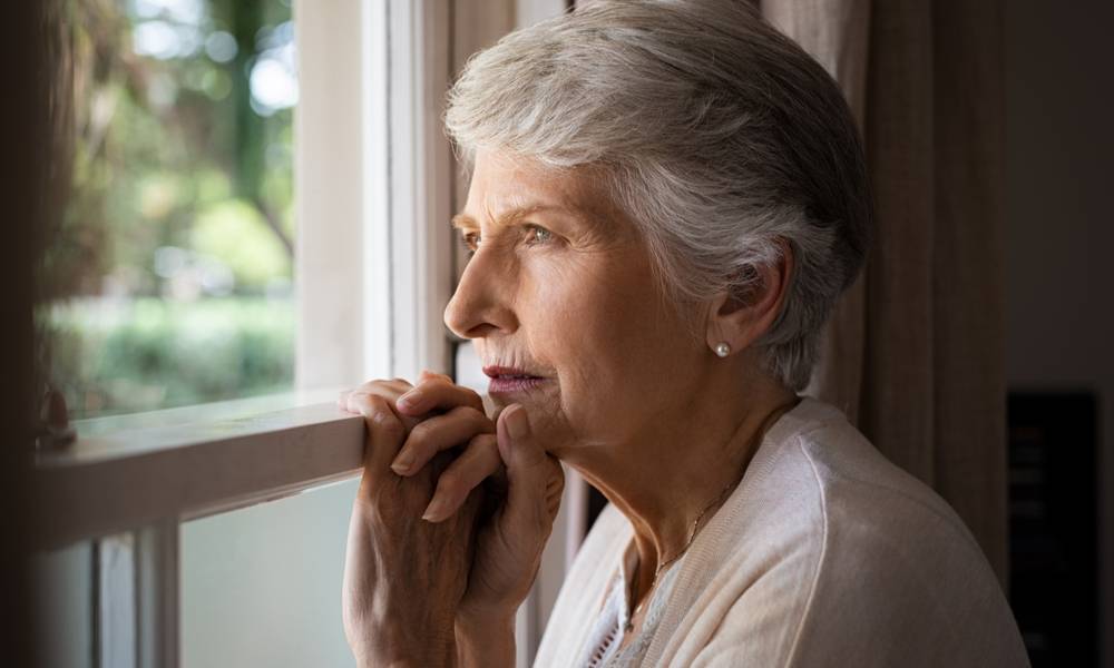 An ageing woman looks out of window depressed.jpeg