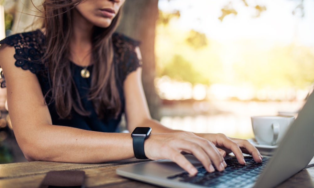 Young woman wearing smartwatch using laptop computer. Female working on laptop in an outdoor cafe..jpg
