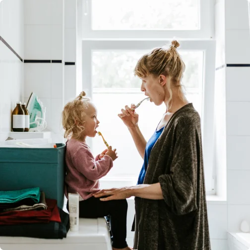 Mother and daughter brush their teeth together.