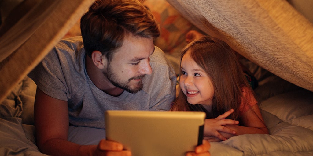 Man and his daughter reading a book and smiling at each other.