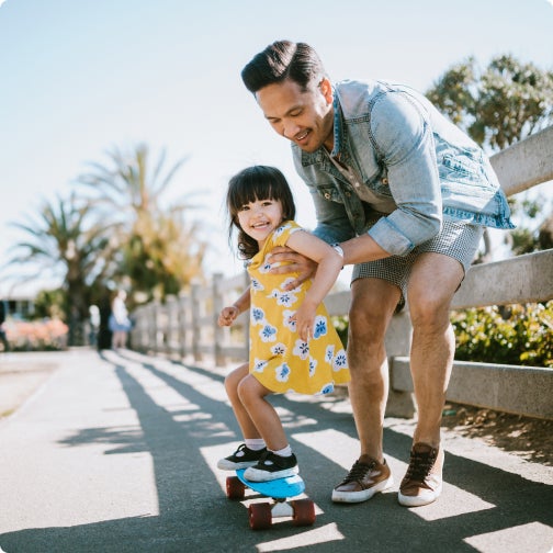 Dad teaching his daughter how to skateboard.
