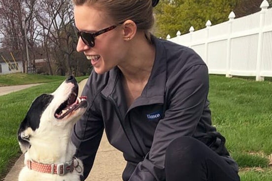 woman and dog both looking at each other smiling on a sidewalk