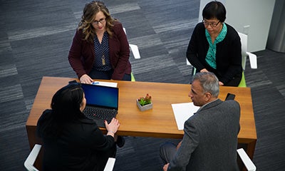 an over head view of three women and a male discussing at a desk