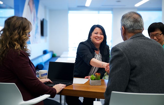 eine Gruppe von Leuten, die an einem Tisch sitzen, während 2 von ihnen sich die Hand geben